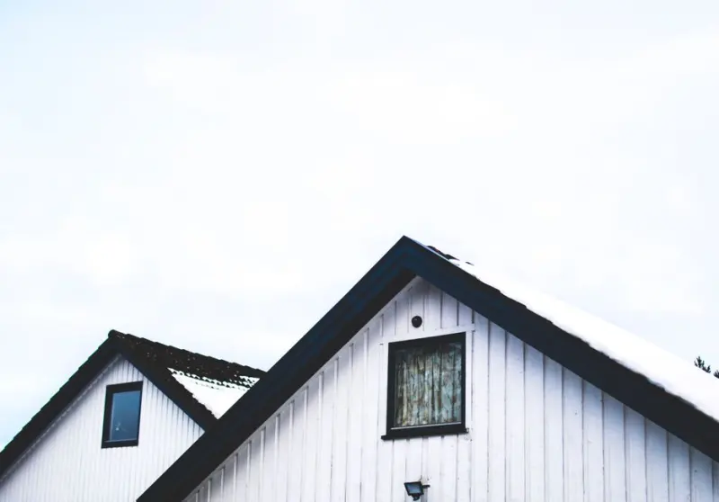 White bungalow roof with snow against a clear sky.